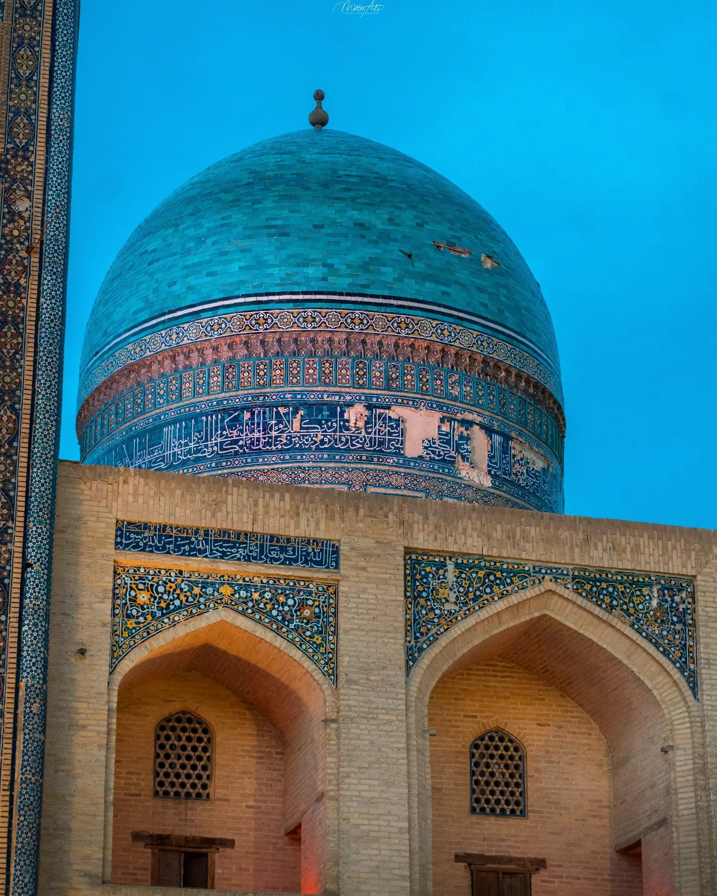 An ornate tiled entrance portal of a mosque lit up at dusk
