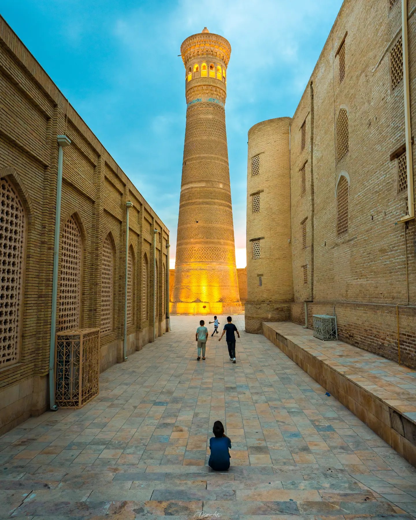 The Kalyan Minaret and a mosque entrance at dusk with a person sitting nearby