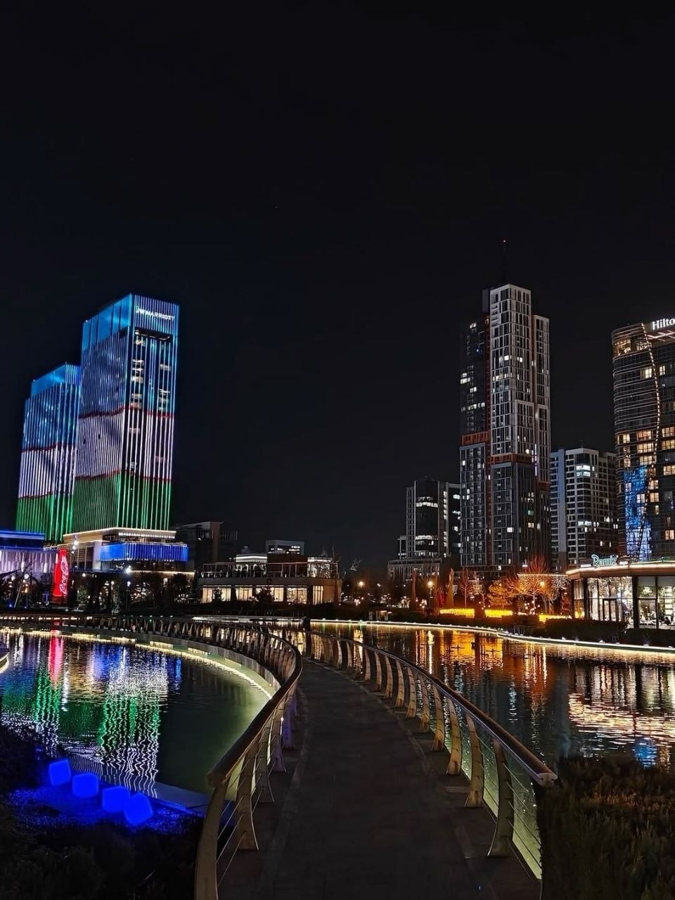 Tashkent city skyline at night, with illuminated buildings reflecting in a canal